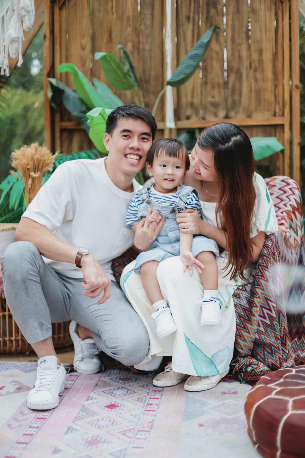 Loving Asian family with baby sitting together in a boho outdoor photo setting.