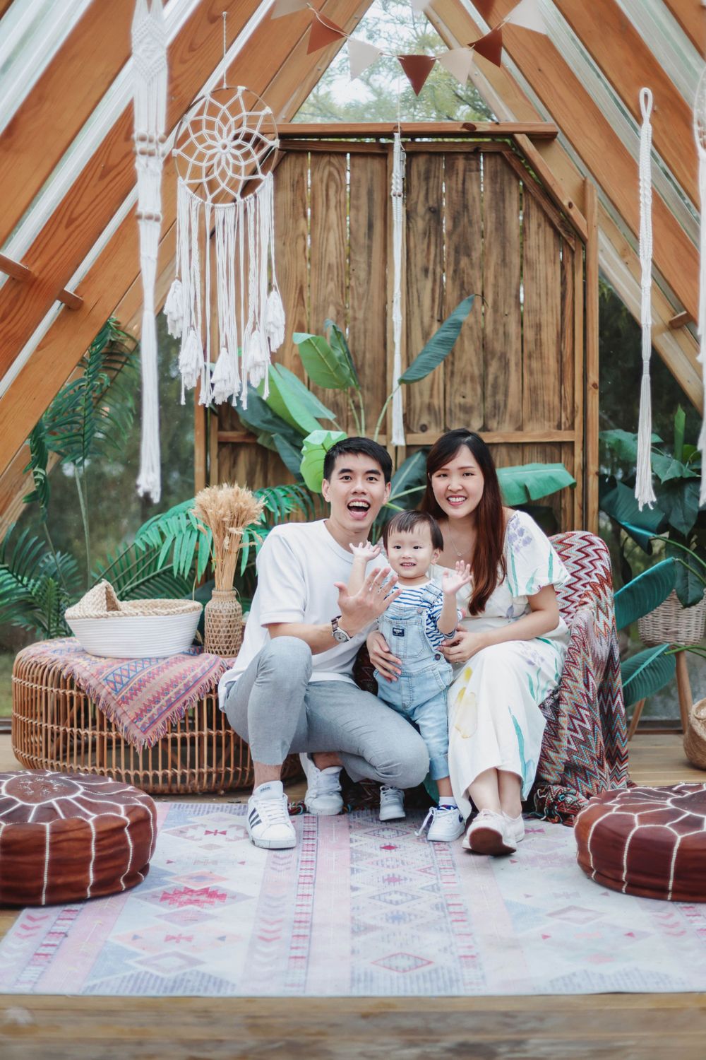 Happy Asian family with baby sitting together in a bohemian A-frame decorated space with dreamcatchers.