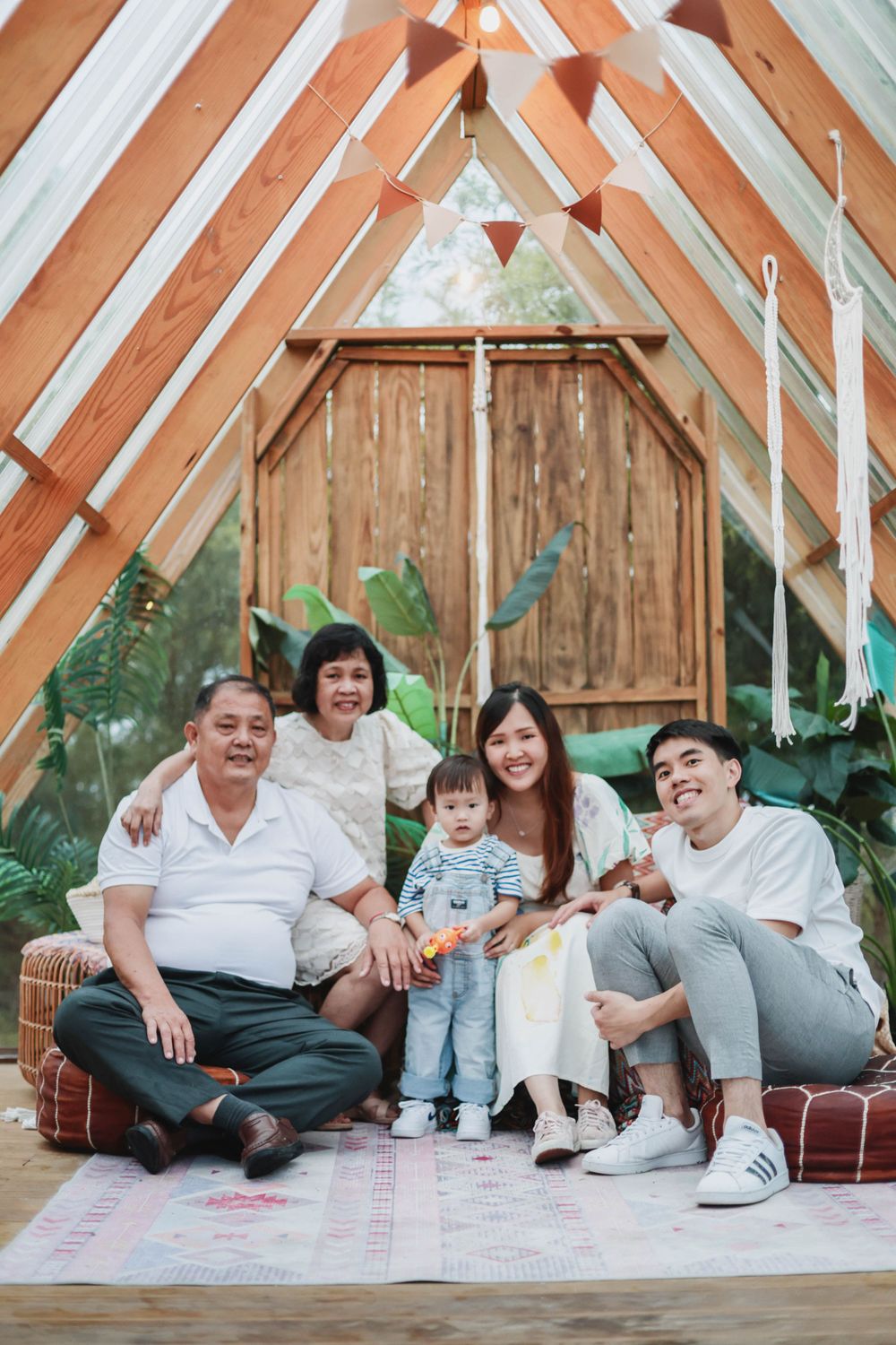 Multi-generational Asian family with grandparents, parents and toddler posing in boho A-frame setting.