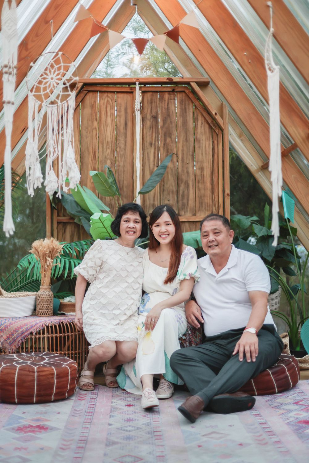 Asian woman with her parents smiling together in a bohemian A-frame decorated outdoor space.