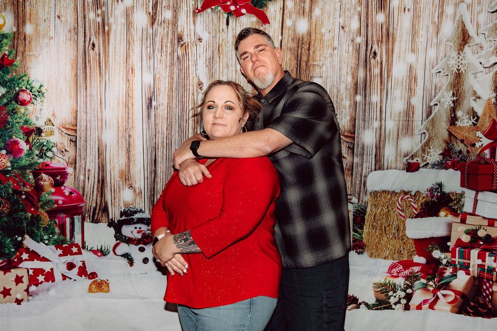 Holiday portrait session with rustic wood backdrop, red poinsettias, and Christmas decorations in warm cozy setting.