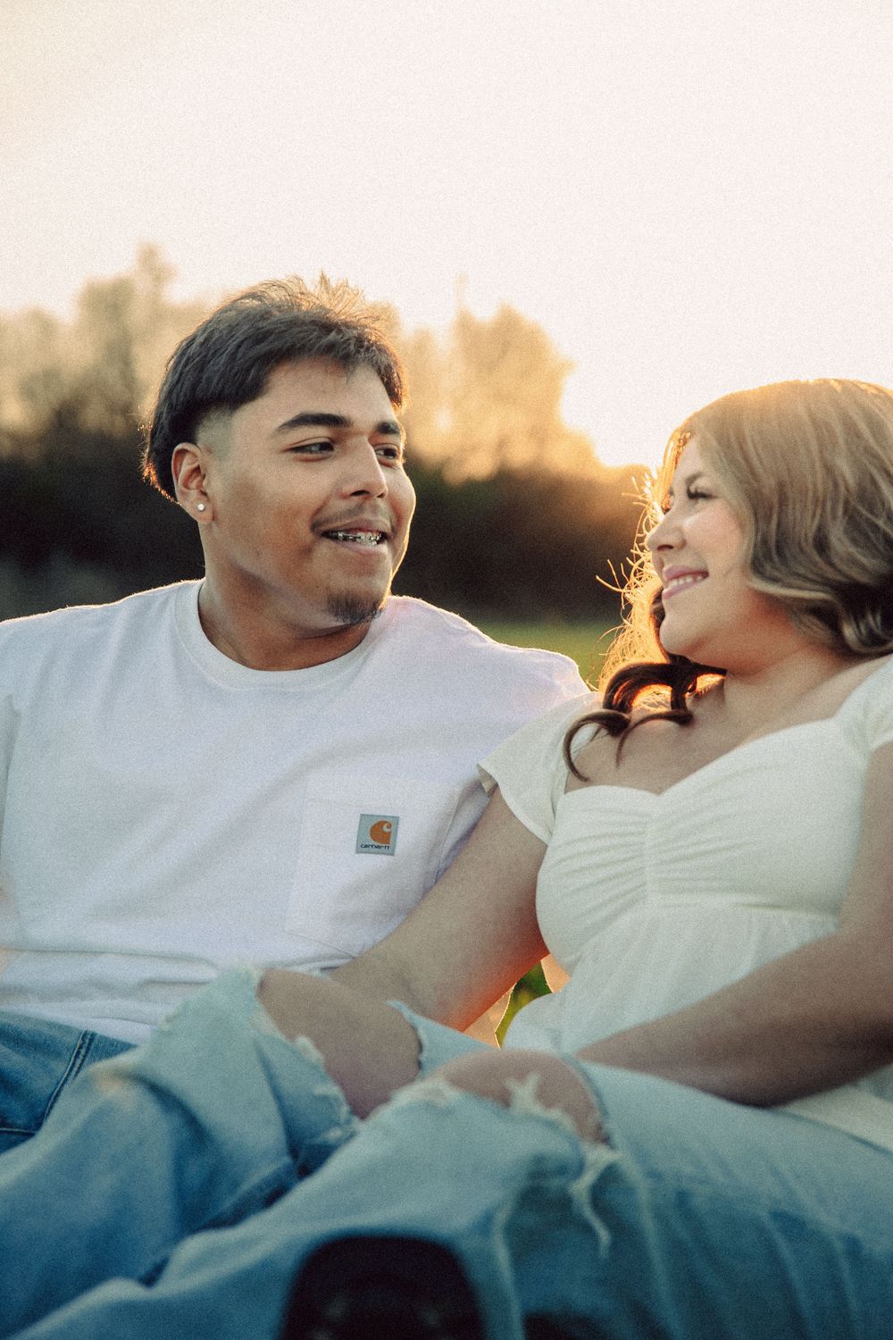 A couple smiles at each other while relaxing outdoors during golden hour.