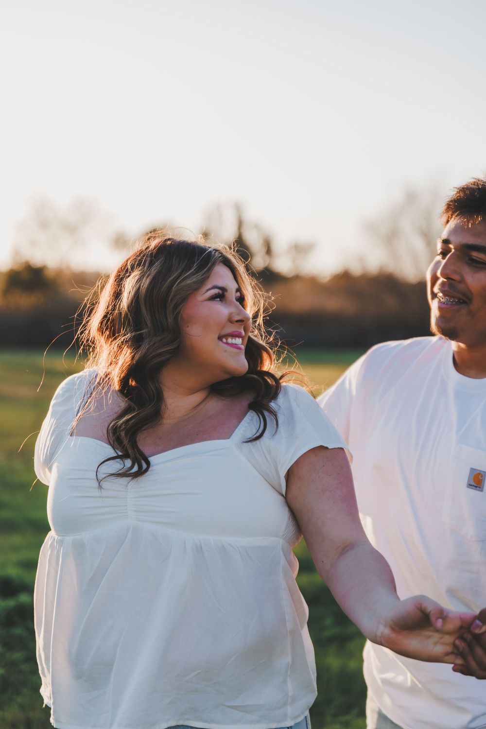 A couple laughs together in a field during a warm sunset photoshoot.