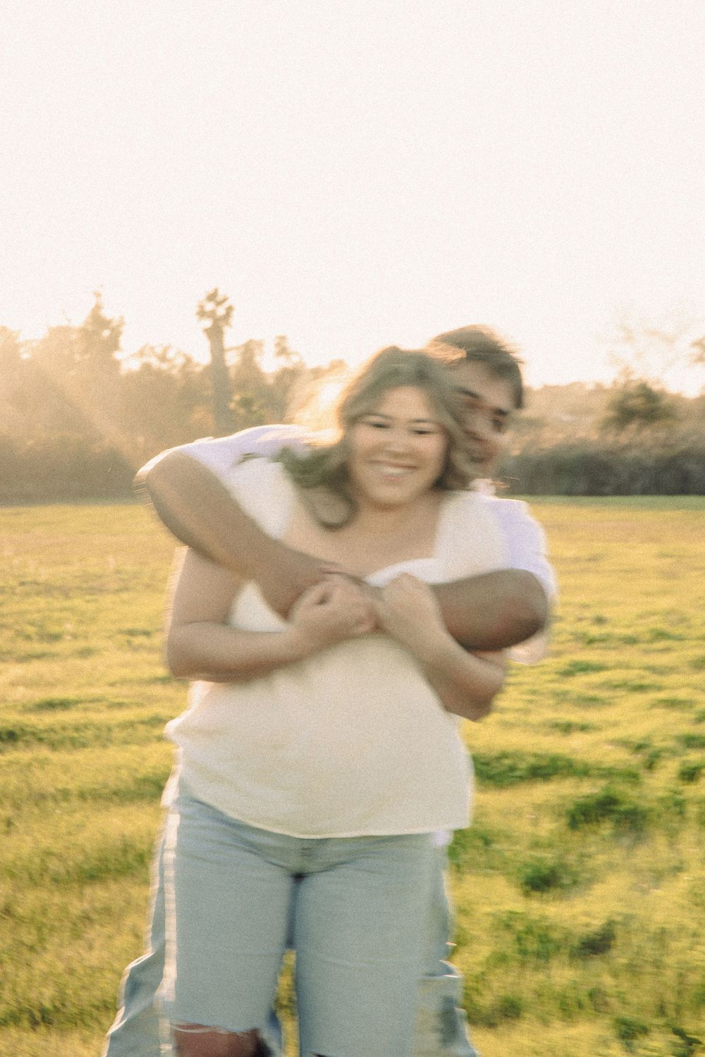 A couple embraces joyfully in a sun-drenched meadow during golden hour, creating a warm and romantic atmosphere.