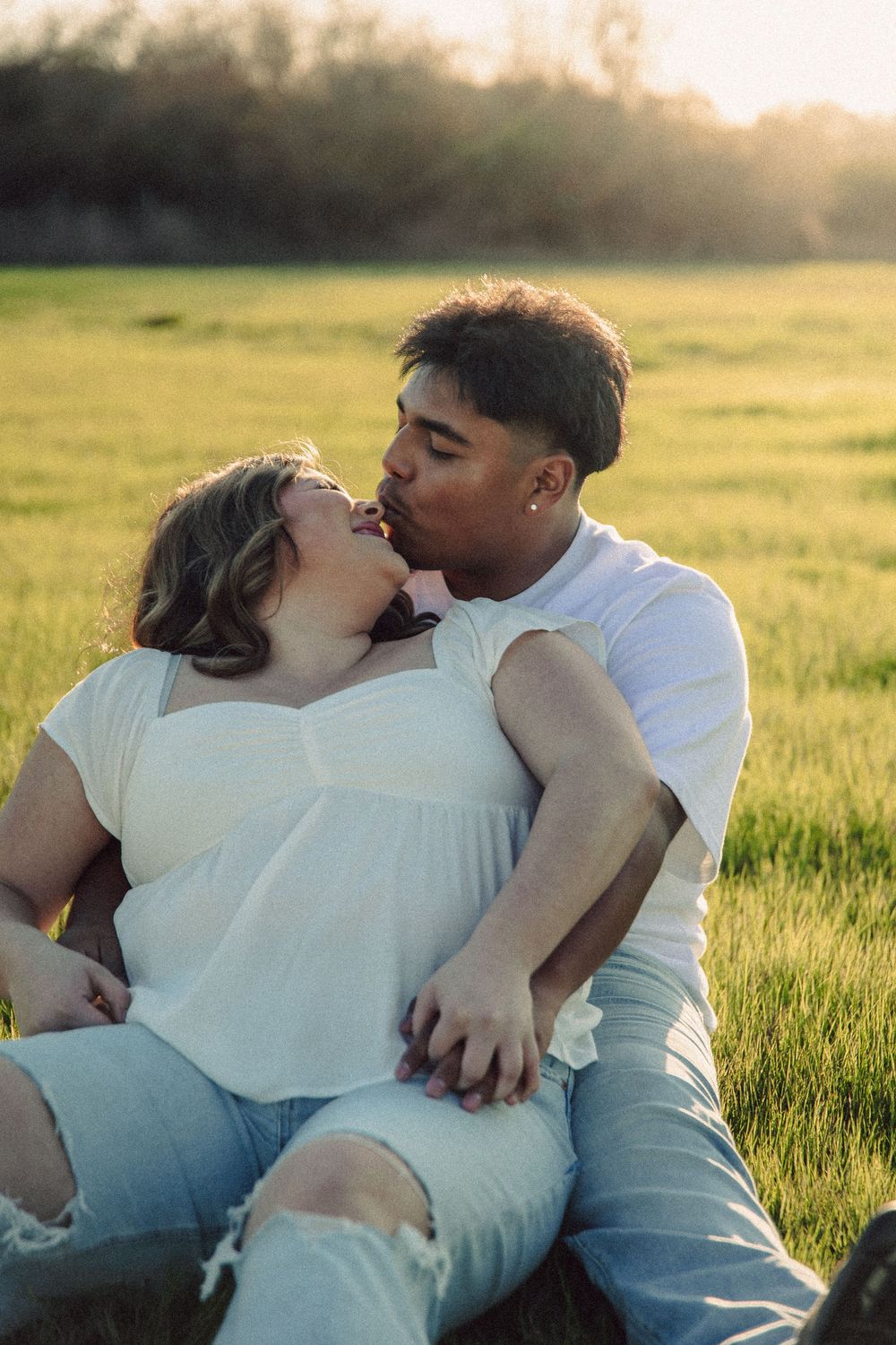 A romantic couple embraces in a sunlit meadow during golden hour.