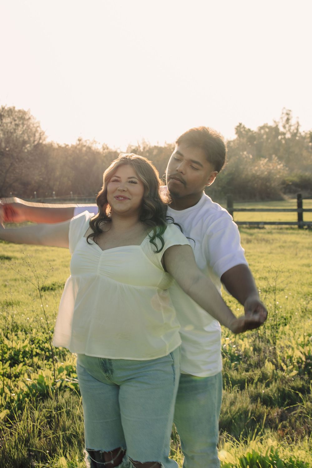 A couple embraces in a sunlit field during golden hour, sharing a joyful moment together in nature.
