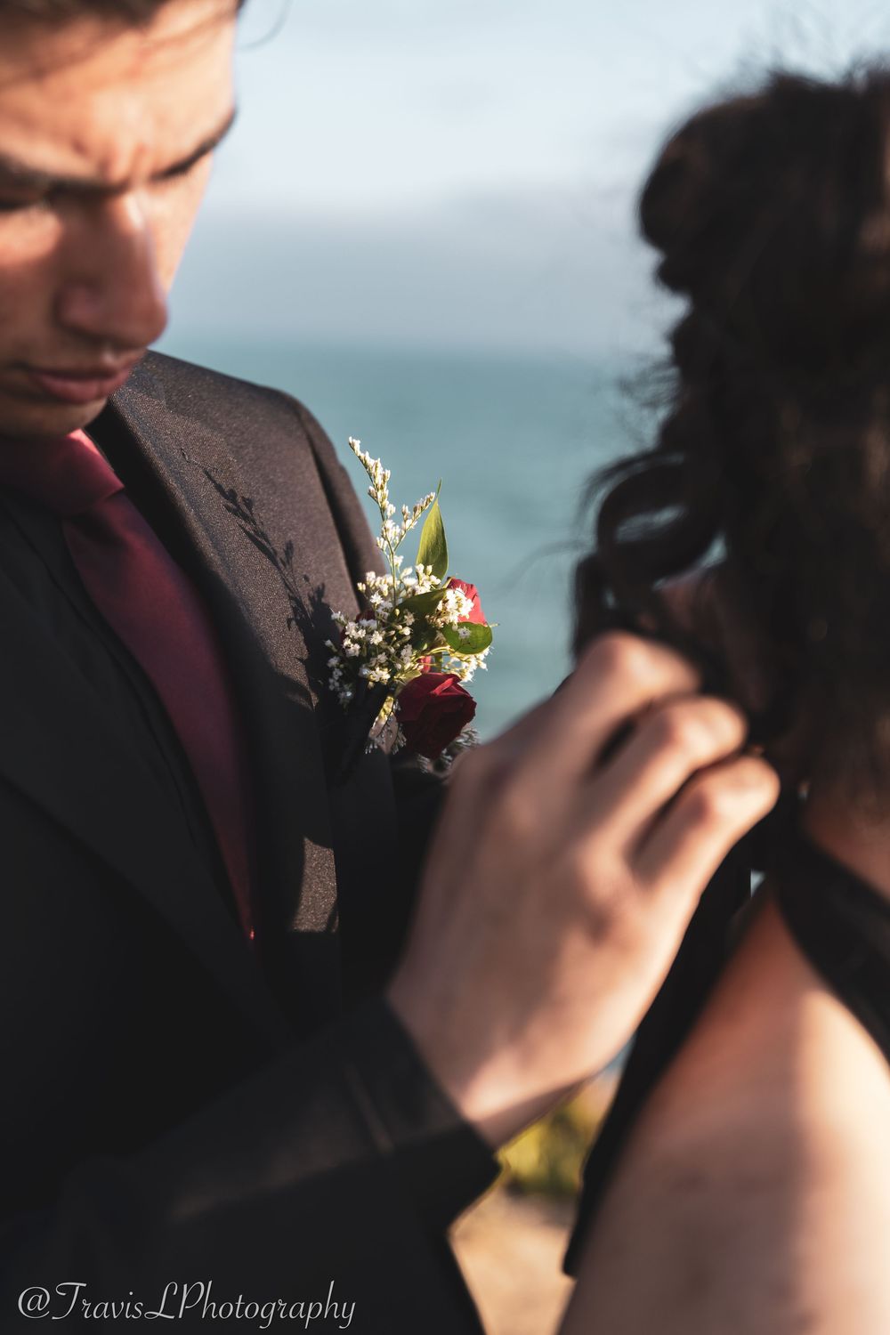 Close-up detail of a burgundy boutonniere with delicate white flowers pinned to a dark suit jacket.