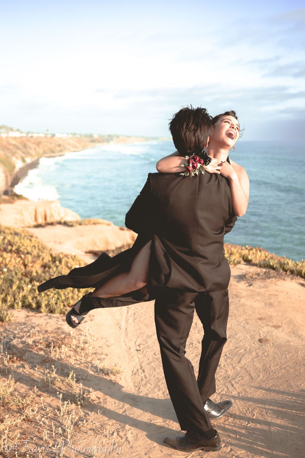 Playful couple dancing together on coastal cliffs overlooking the ocean at sunset.