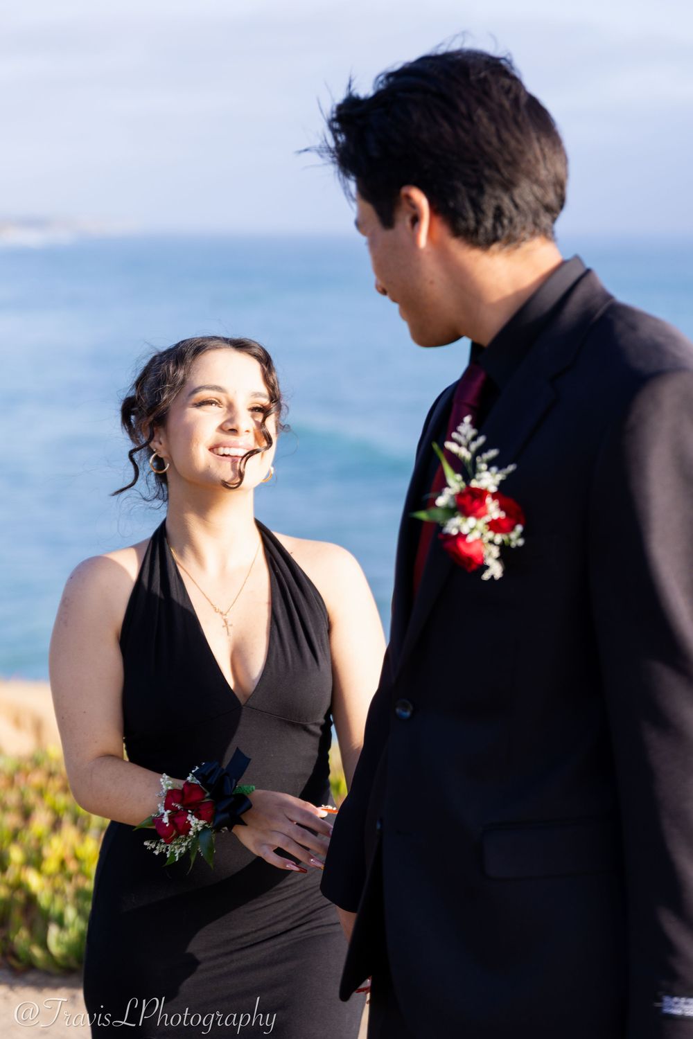 Couple in formal black attire sharing an intimate moment by the ocean.