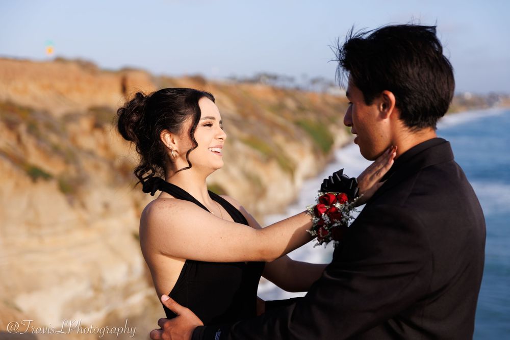 Couple in black formal wear embracing on coastal cliffs with ocean views.
