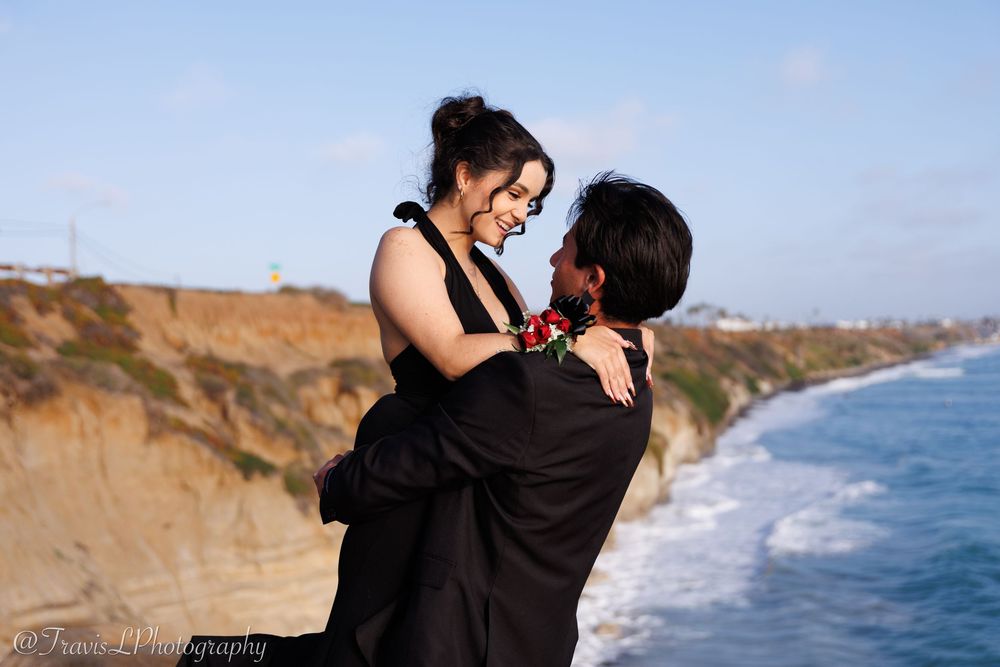 Romantic coastal photoshoot with couple against dramatic ocean backdrop.