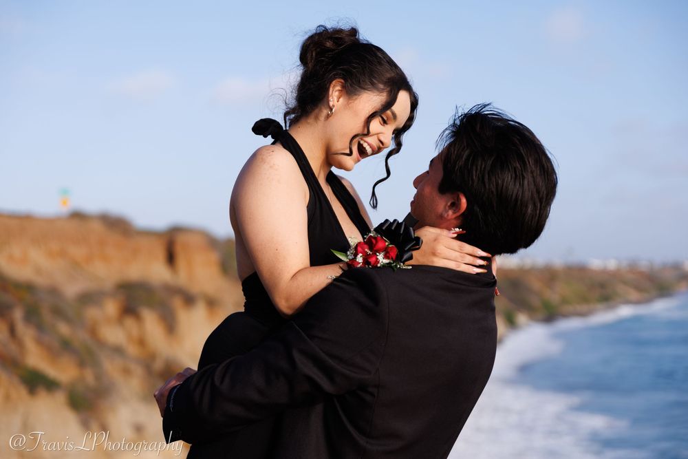 Joyful couple dancing together on oceanside cliff during sunset photoshoot.