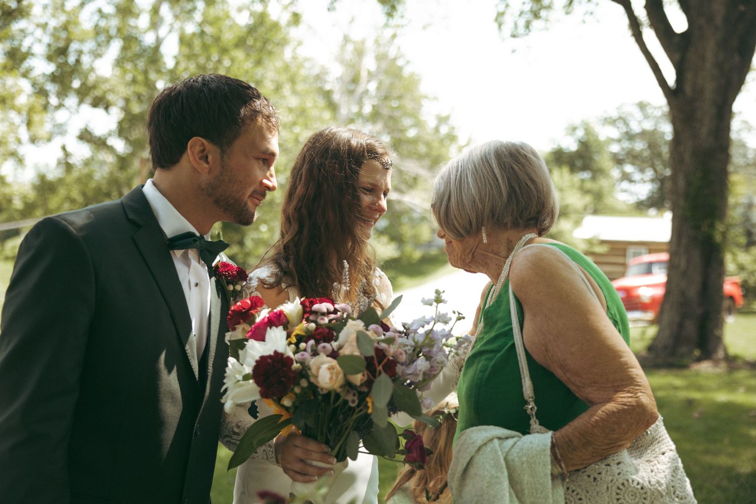 Outdoor wedding gathering with floral bouquets on sunny garden lawn.