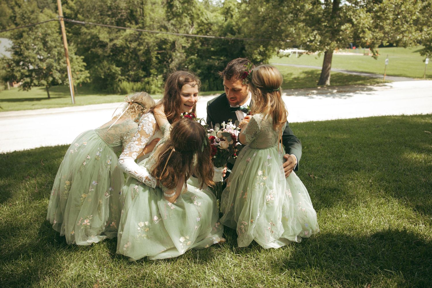 Group in mint green dresses gathering on sunny lawn during wedding celebration.