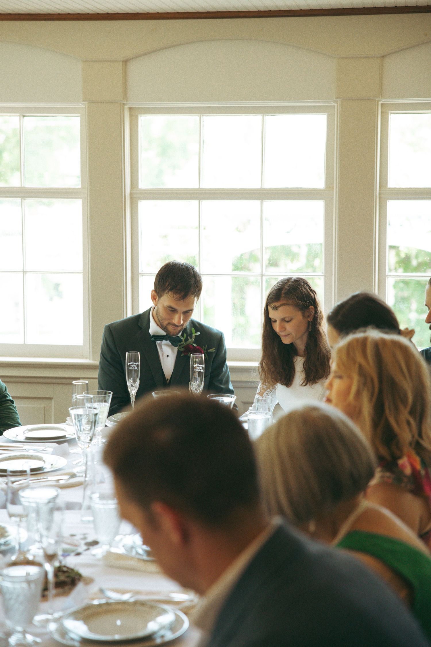 Wedding reception in bright dining room with formal place settings and large windows.