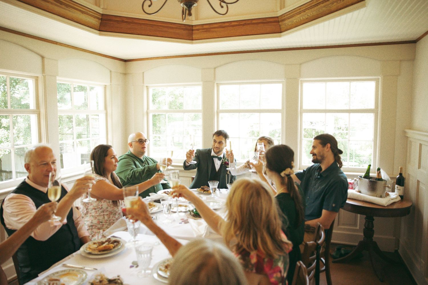 Wedding guests toasting at elegant indoor reception with bright windows.