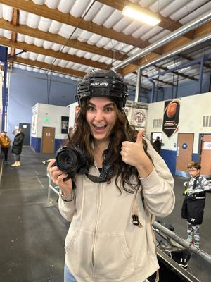 A photo of Brenna wearing a hockey helmet and smiling with her camera