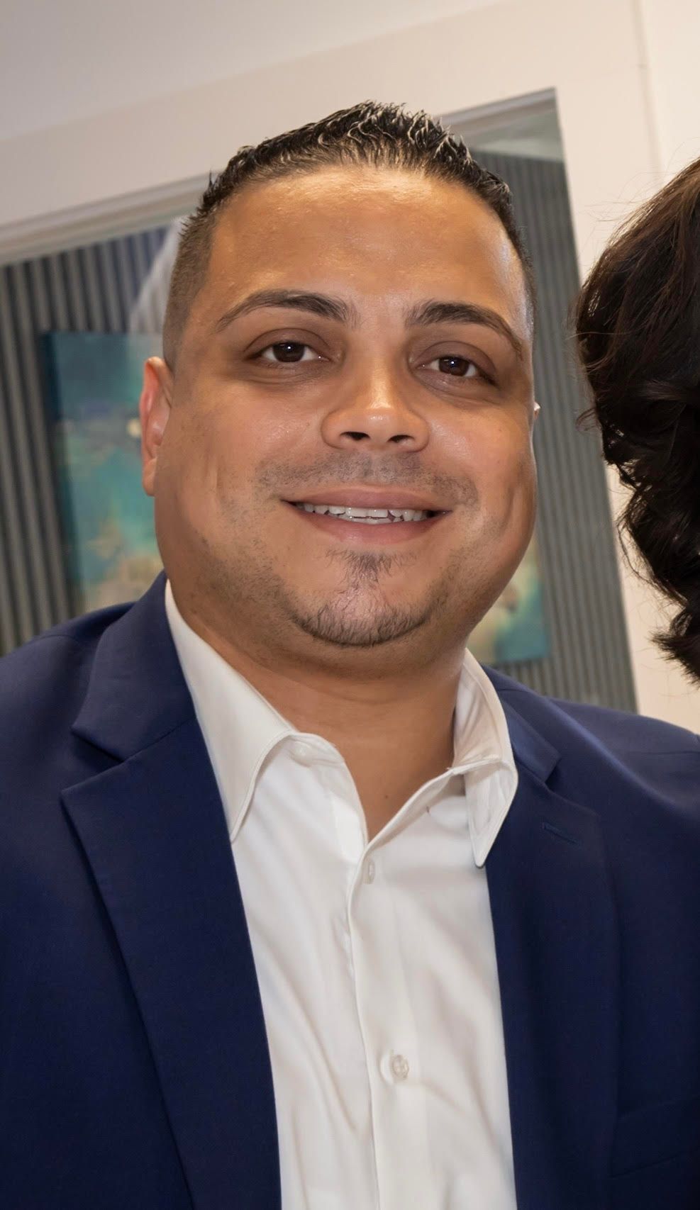 Professional studio headshots of a man in a navy suit and white dress shirt against a soft focus background.