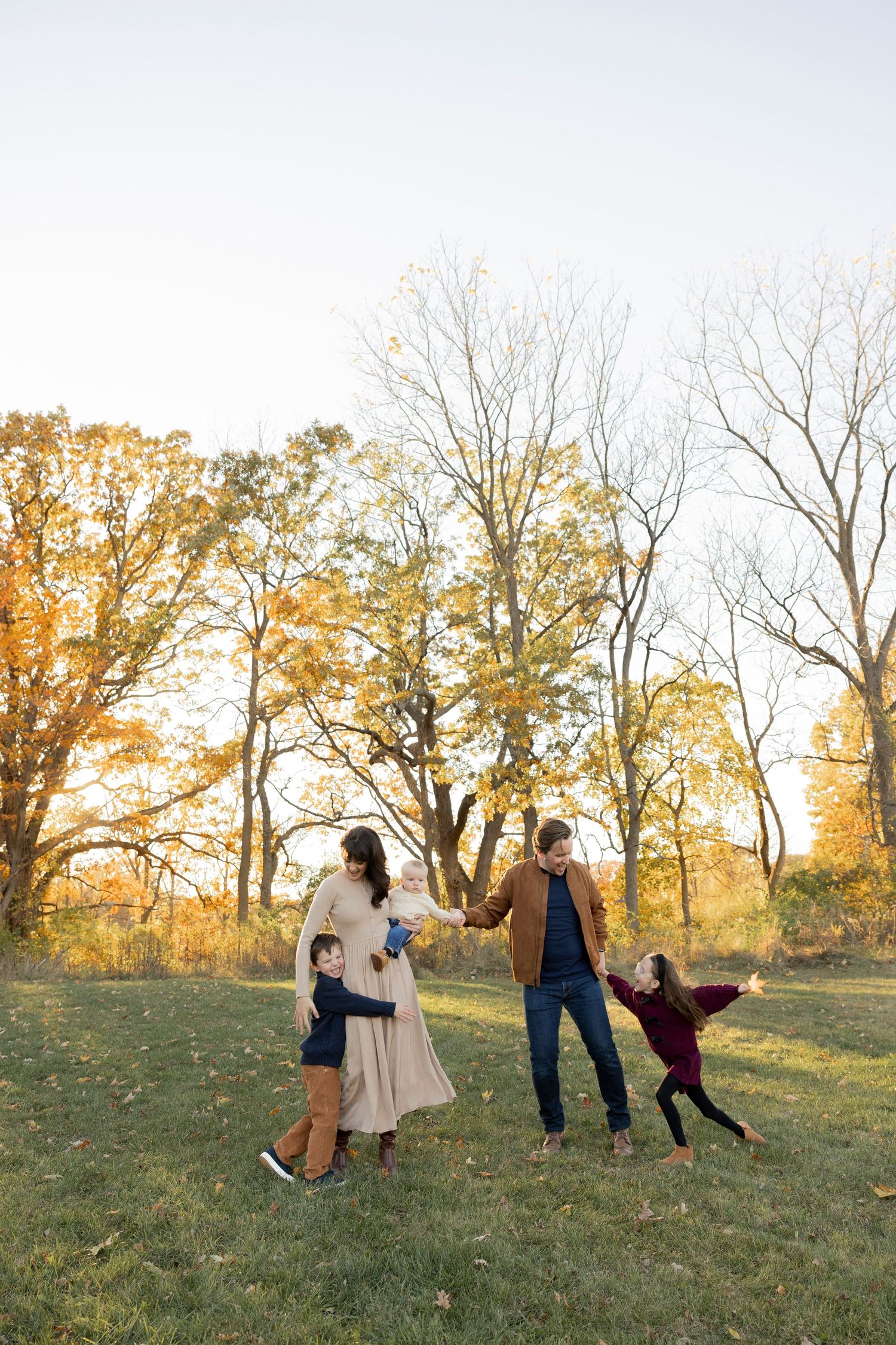 A family playing together in a grassy field at sunset with autumn trees creating a golden backdrop at bear creek in Rochester Hills michigan