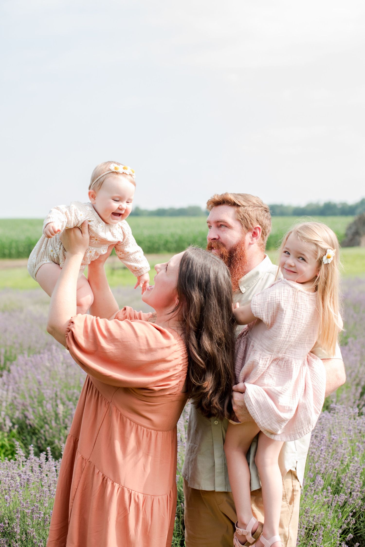 Joyful family of four plays together in blooming lavender field during outdoor summer family portraits.