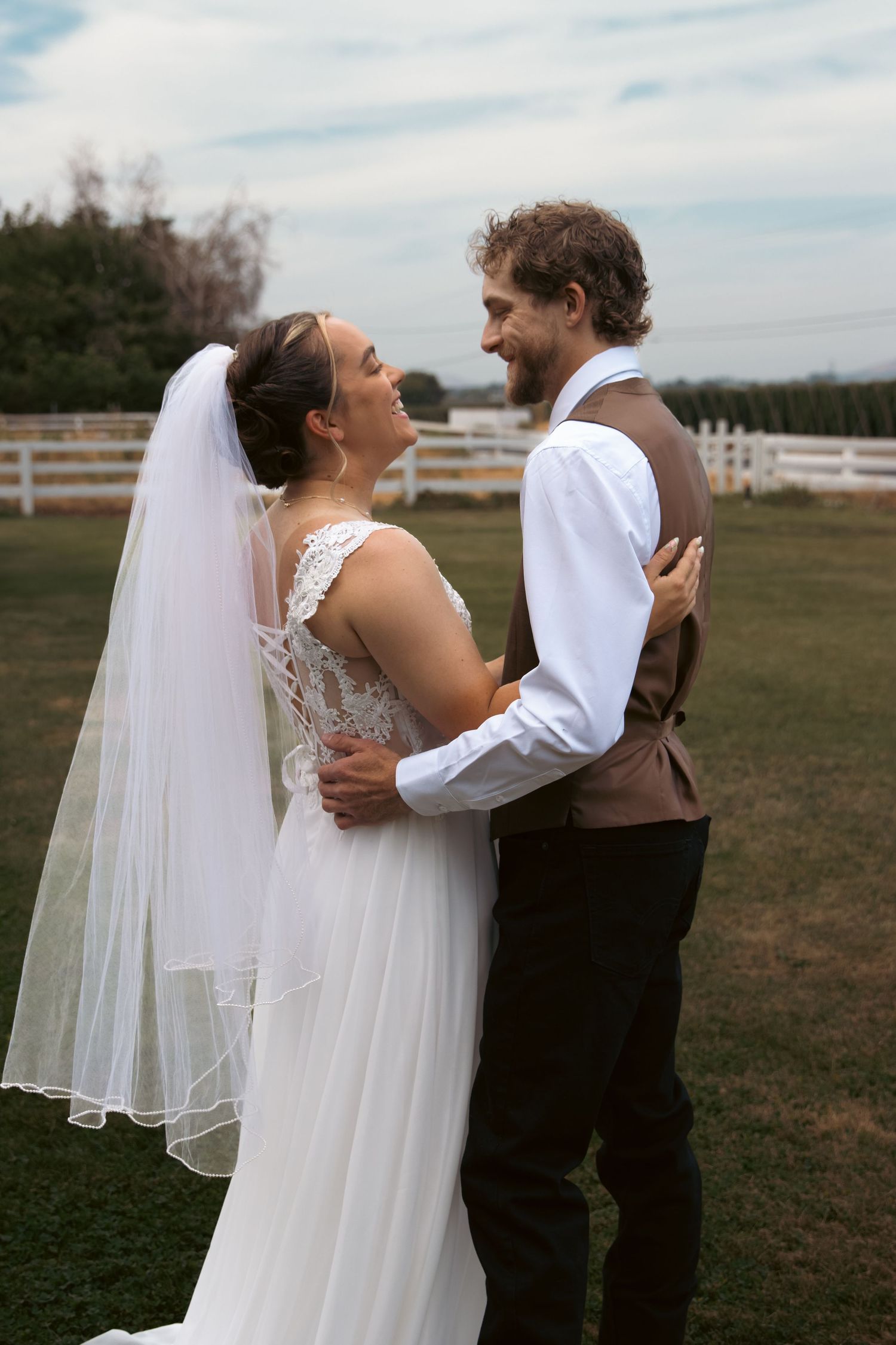 Bride and groom embrace and smile at each other in a farm setting on their wedding day.