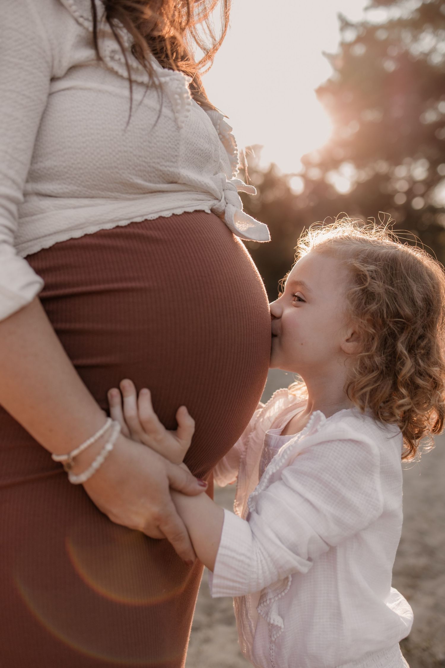 Warm en puur gefotografeerd moment met grote zus tijdens zwangerschapssessie in de natuur.