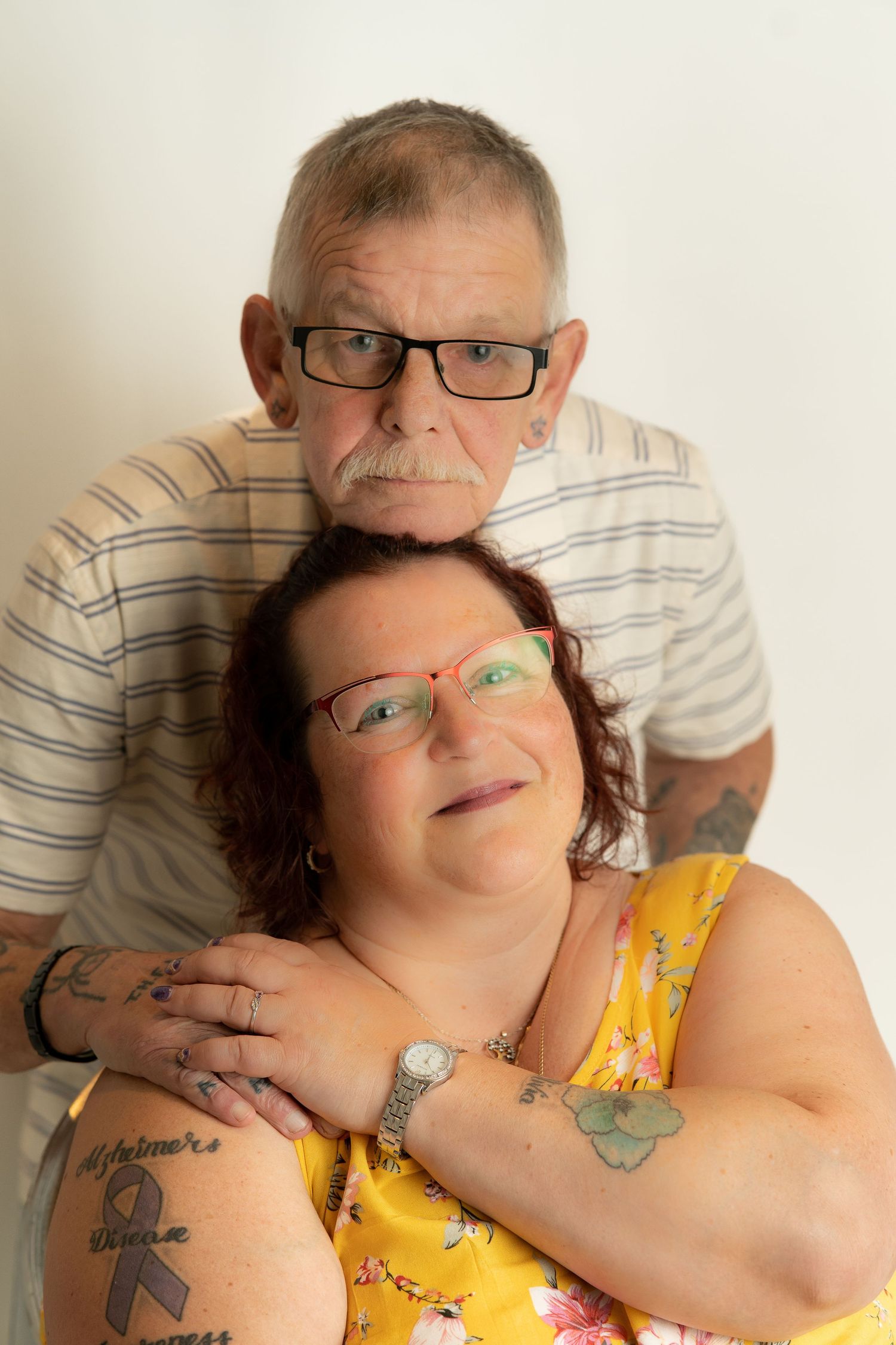Portrait of couple embracing against white background showing matching tattoos.
