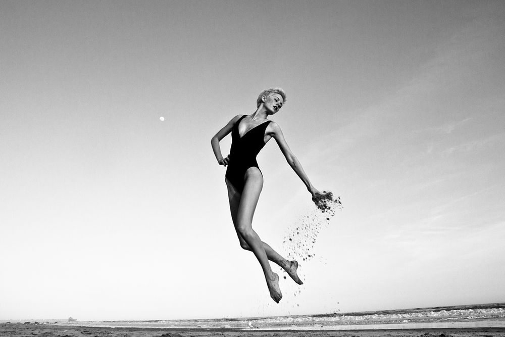 Dancer creates dreamlike scene while leaping on beach in artistic black and white photo.