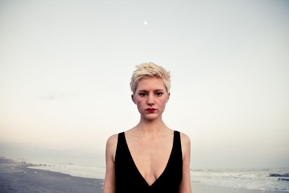 Figure in black swimsuit stands against serene ocean backdrop at sunset with full moon in the distance.
