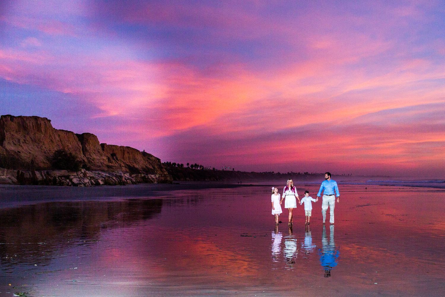 Silhouettes of a family walking on a beach at sunset with vibrant purple and orange sky.