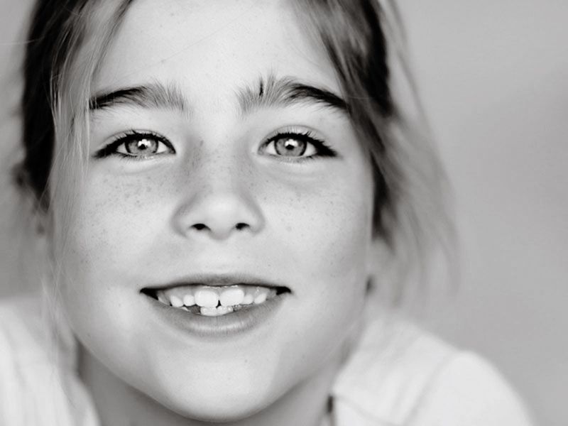 Four black and white close-up portraits show a child's smiling face and expressions in a playful photo series.