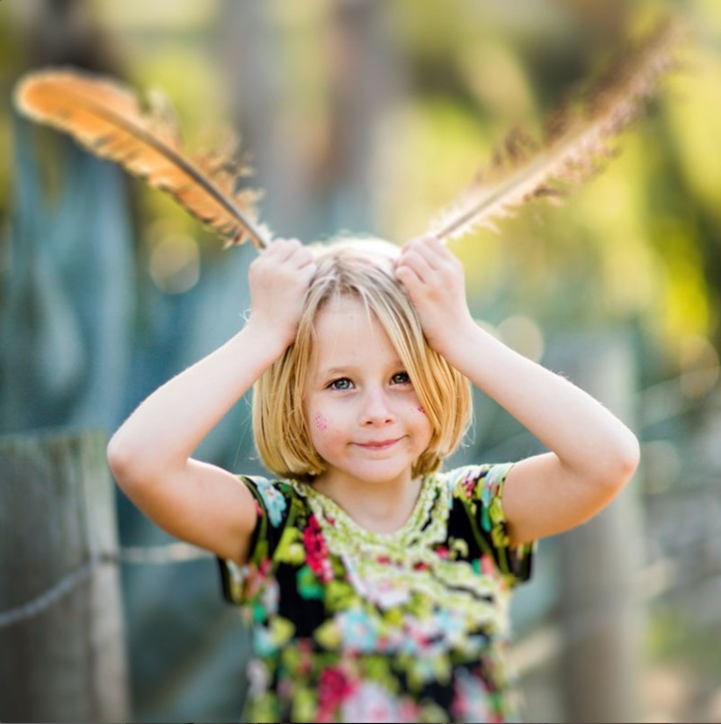Child playing with feathers as pretend antennae outdoors in floral dress.