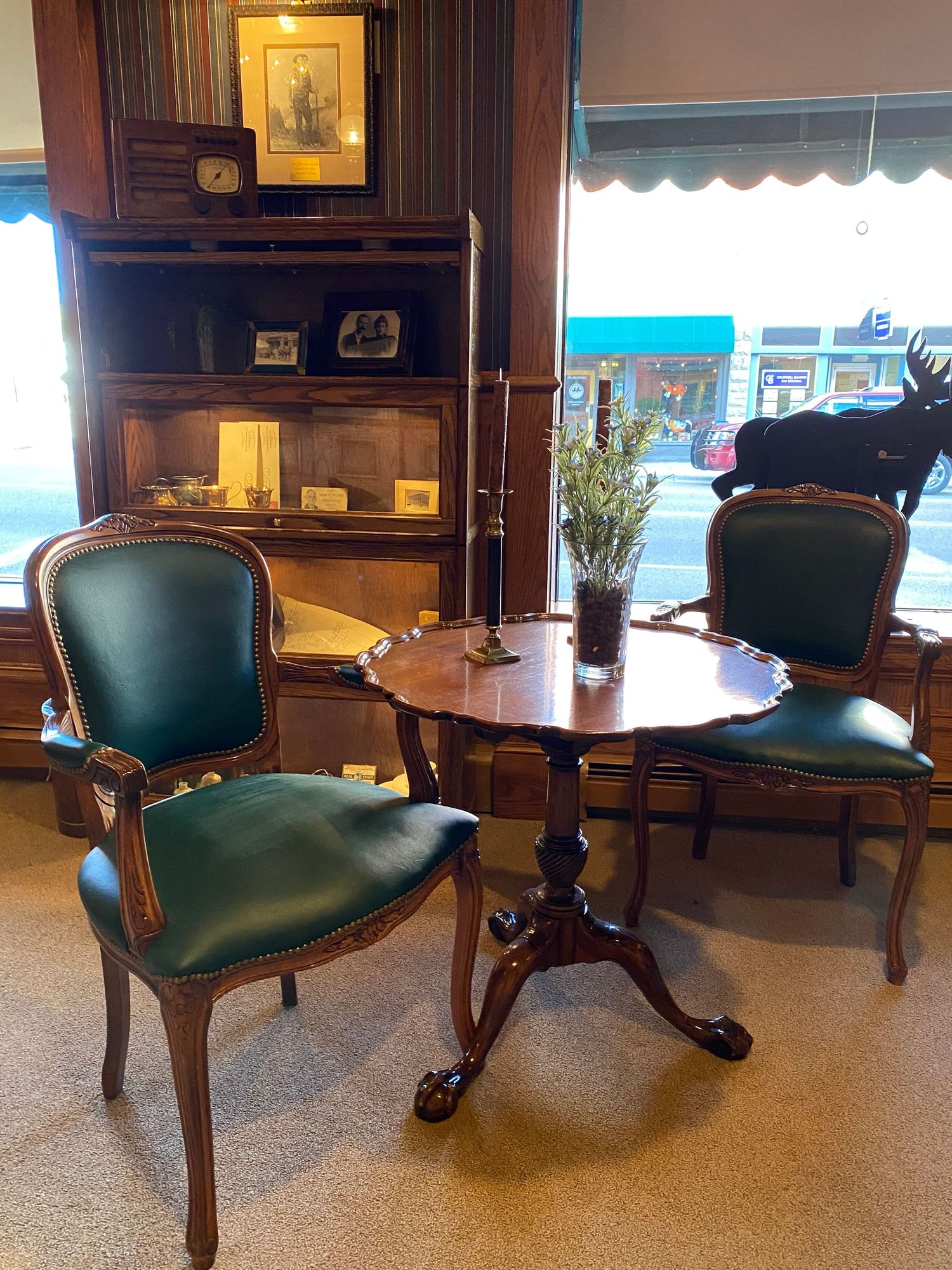 Elegant vintage sitting area with green leather chairs and round table near a window.