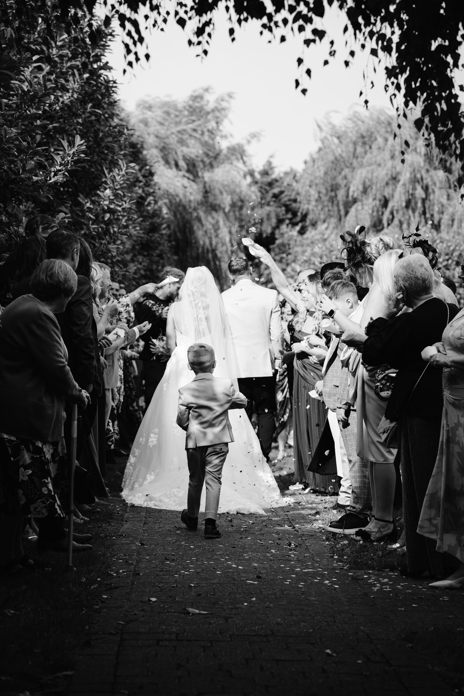 Bride and groom walk through confetti tunnel as guests celebrate their outdoor wedding ceremony exit.