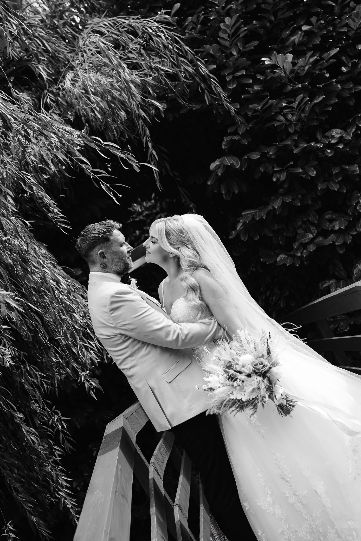 Bride and groom sharing a romantic kiss outdoors in black and white wedding photo.