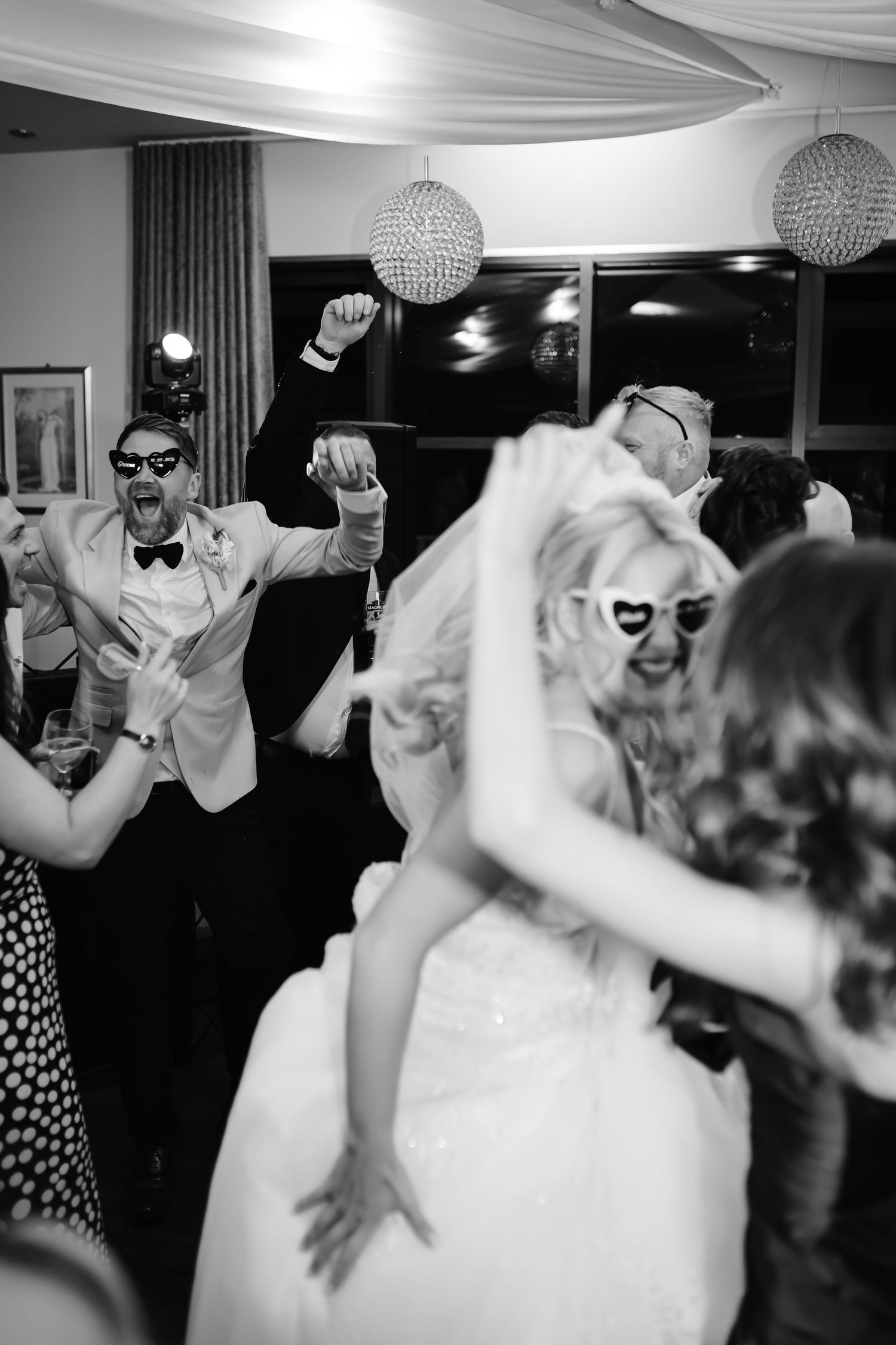 Bride and groom dancing joyfully with sunglasses at a lively black and white wedding reception party.