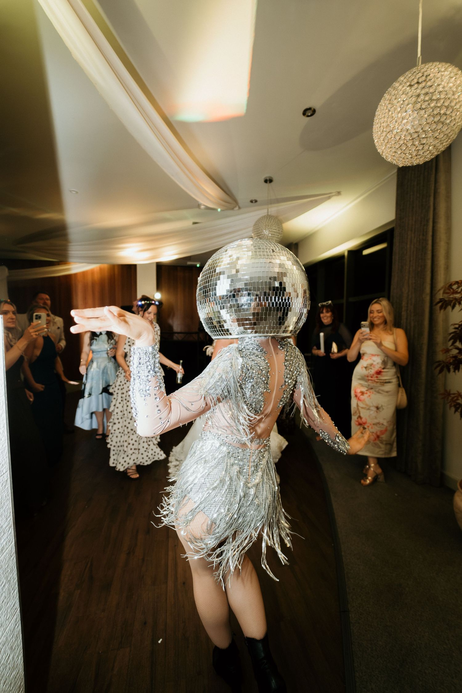 A performer wearing a silver disco ball head and sparkly fringe dress dances at a glamorous wedding reception.