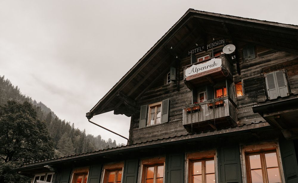 Traditional dark wood Alpine chalet building with warm glowing windows on an overcast day.
