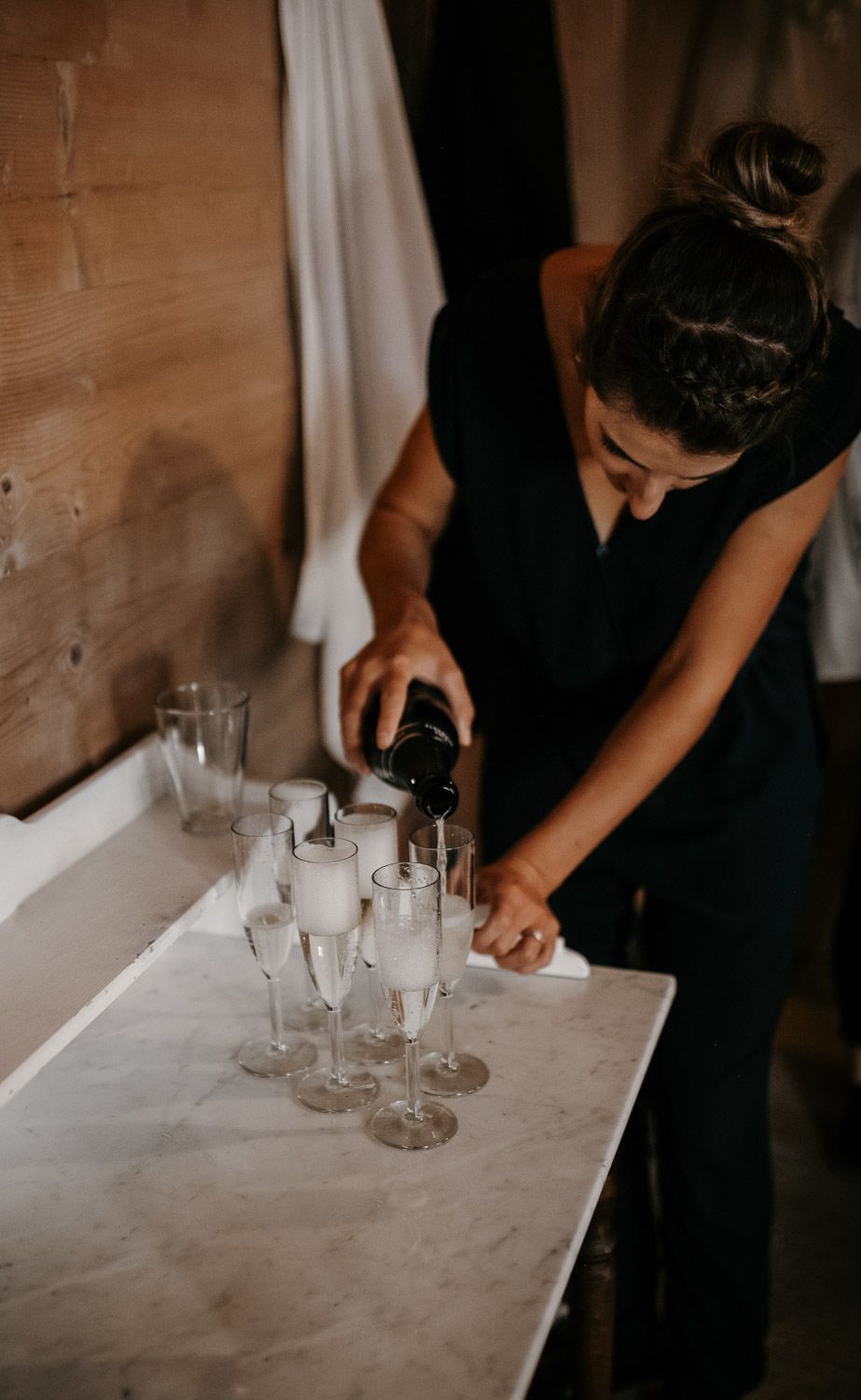 Wedding staff member pouring champagne into elegant flute glasses on a marble-topped table.