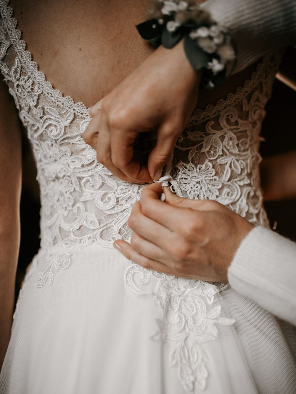 Hands fastening buttons on the back of a white lace wedding dress.