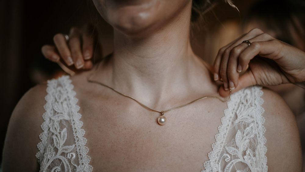 Bride wearing a pearl pendant necklace with a white lace wedding dress.