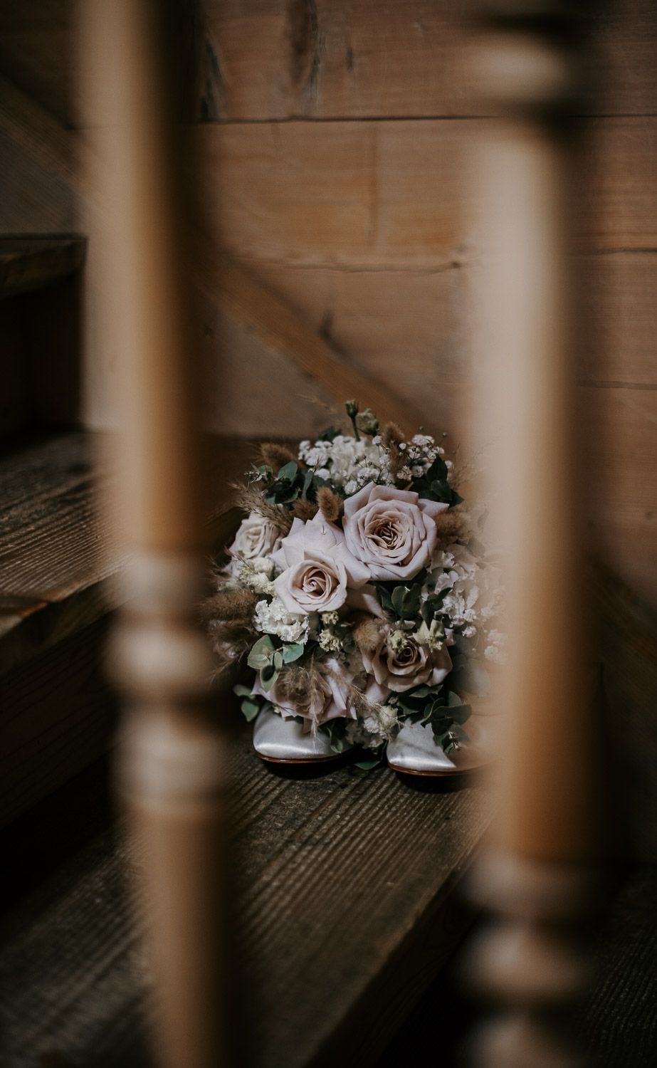 Romantic bridal bouquet of blush roses and greenery resting on wooden stairs, framed by spindles.