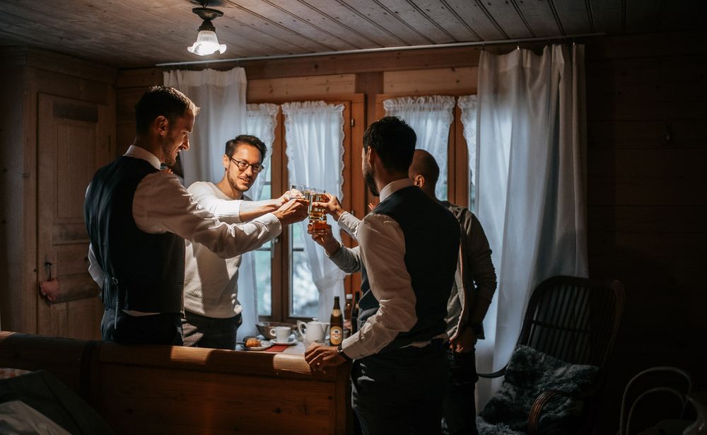 Groomsmen toasting with drinks in a cozy rustic wooden room before the wedding ceremony.