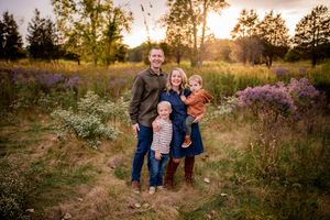 People gather outdoors during golden hour in a scenic natural setting with tall grass and wildflowers at sunset.