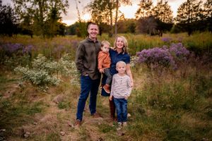 A family of four poses together in a wildflower field at sunset.