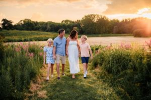 Family walking together through tall grasses at sunset in a summer meadow.