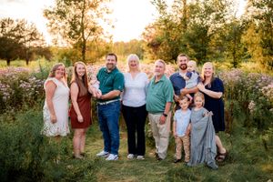 Large family group poses together outdoors in a meadow at sunset.