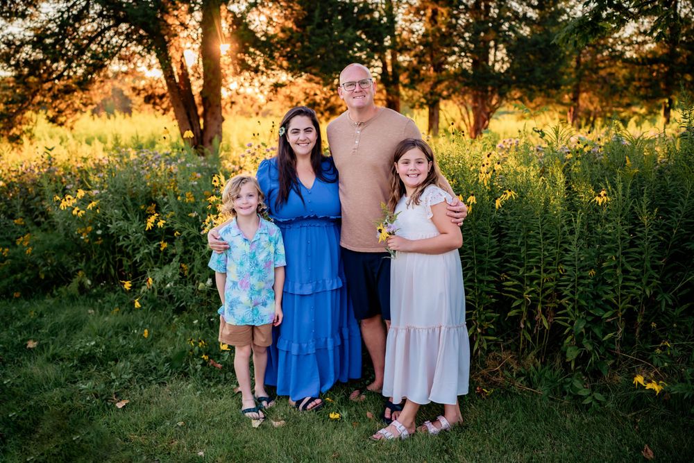 Family poses together in golden sunlight against wildflowers and trees.
