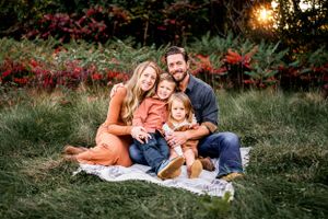 A family sits together on a blanket during golden hour with red foliage in background.