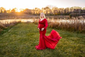 A maternity portrait featuring a flowing red dress in a golden sunset field.